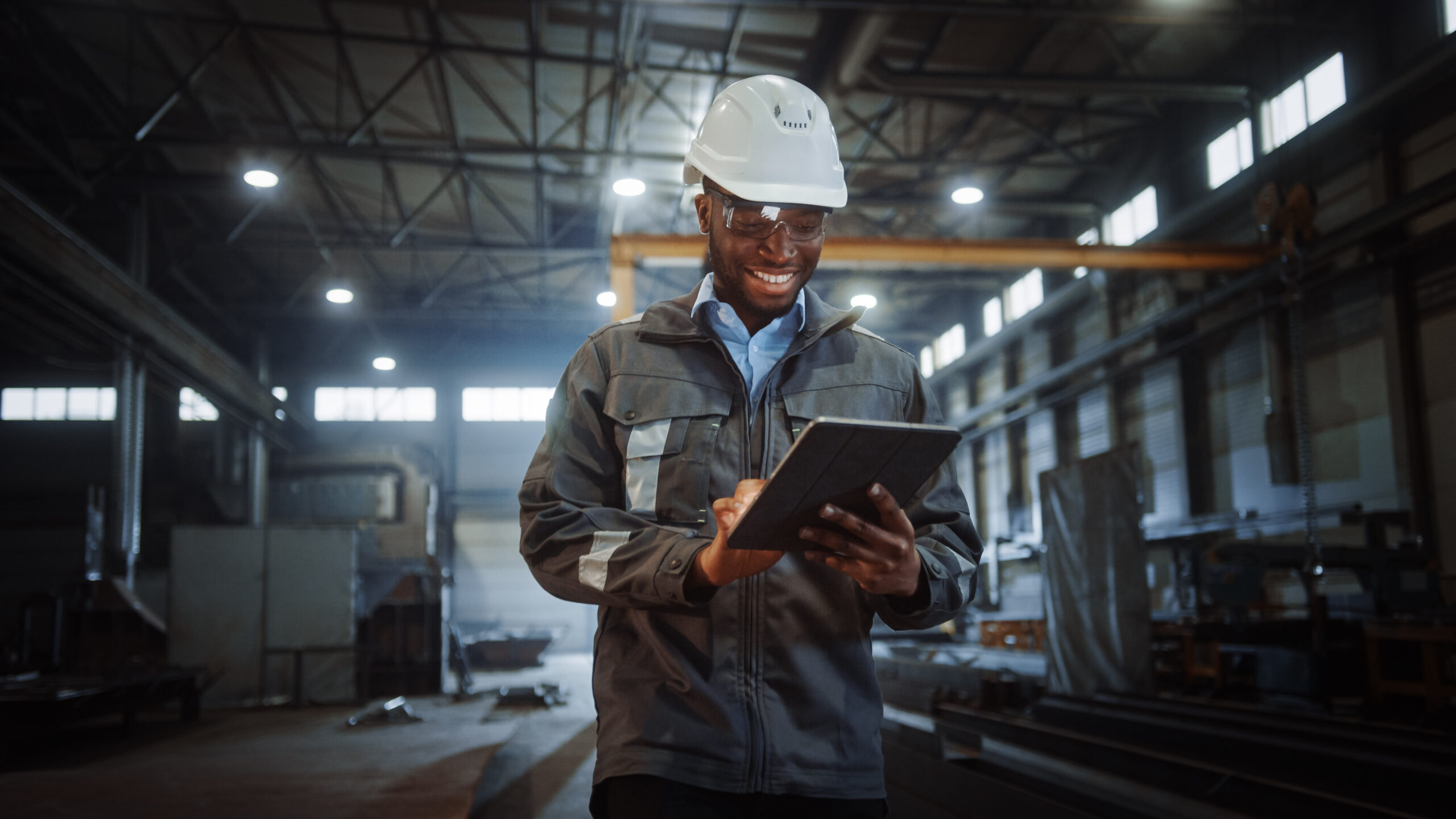 man in hard hat, looking at tablet walking through factory